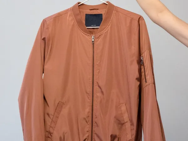 A bomber jacket held up on a hanger against a plain wall