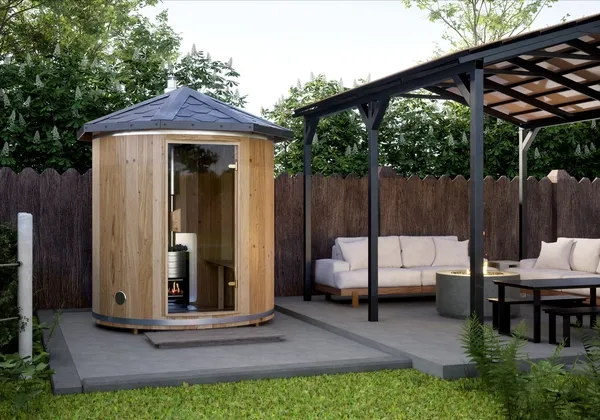 An outdoor barrel sauna on a patio beside a pergola seating area